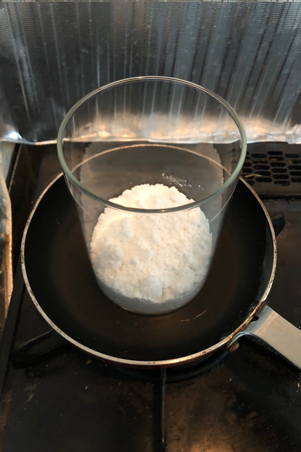 加熱用にフライパンの上にガラス容器を載せ、中身に酒石酸水素カリウムを入れている画像