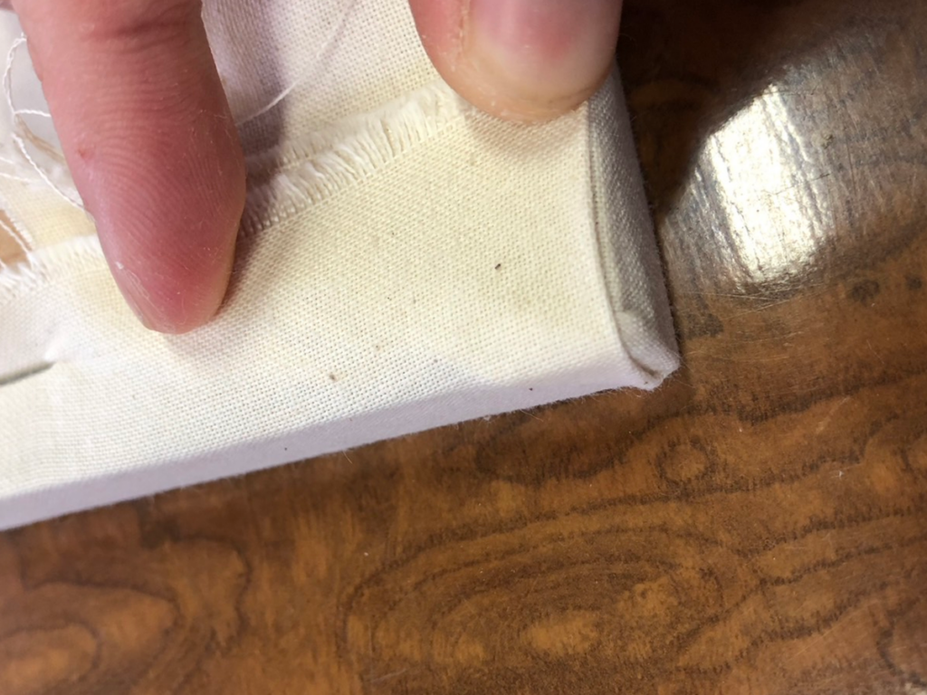 折り込んだ角の布を木枠の裏側へパタンと畳み、タッカーで最終的に固定する様子。角がボコボコしないように処理する職人芸の工程。