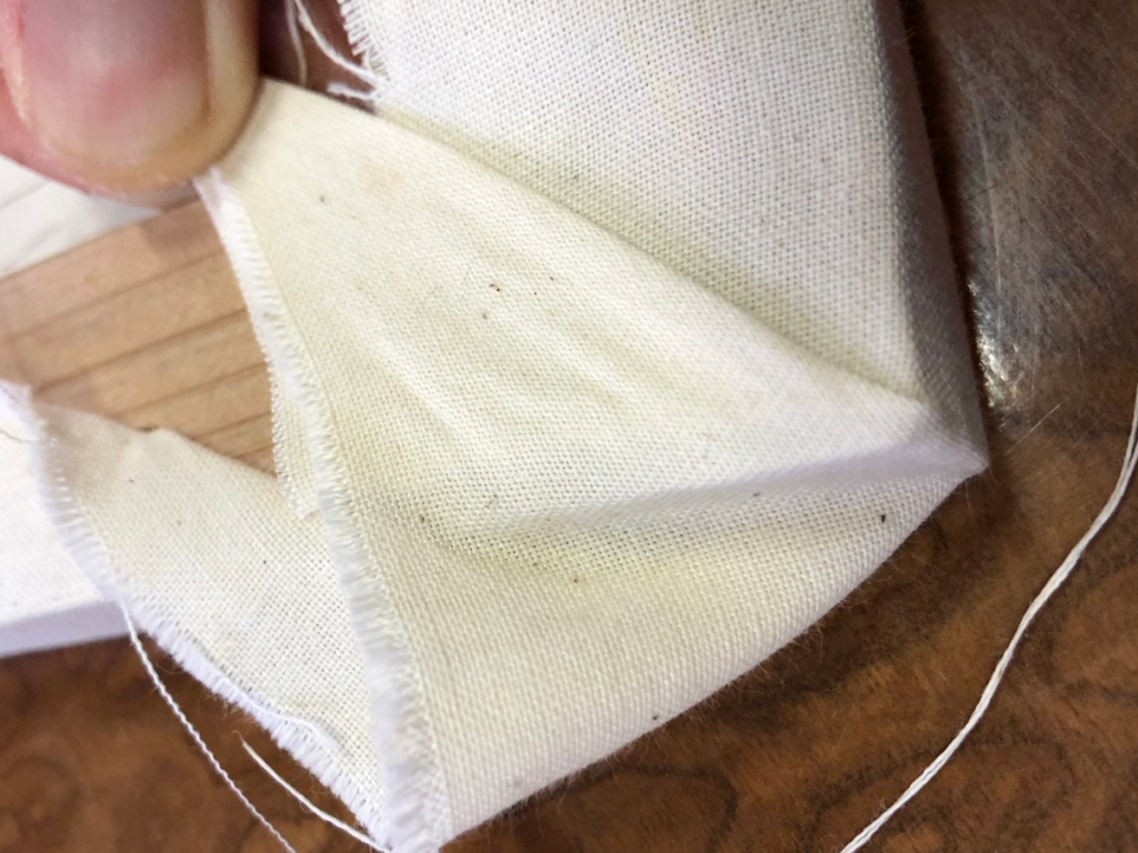 角の余った布を45度に折り込み、厚みが出ないように整えている様子。美しい仕上がりのための三角折りの下準備。