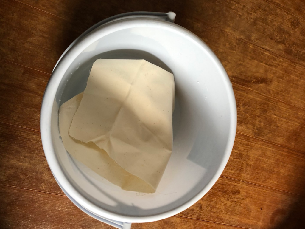 カットした布を水の入ったバケツに浸して水通しをしている様子。あらかじめ繊維を縮ませ、後のたるみを防ぐための下処理工程。