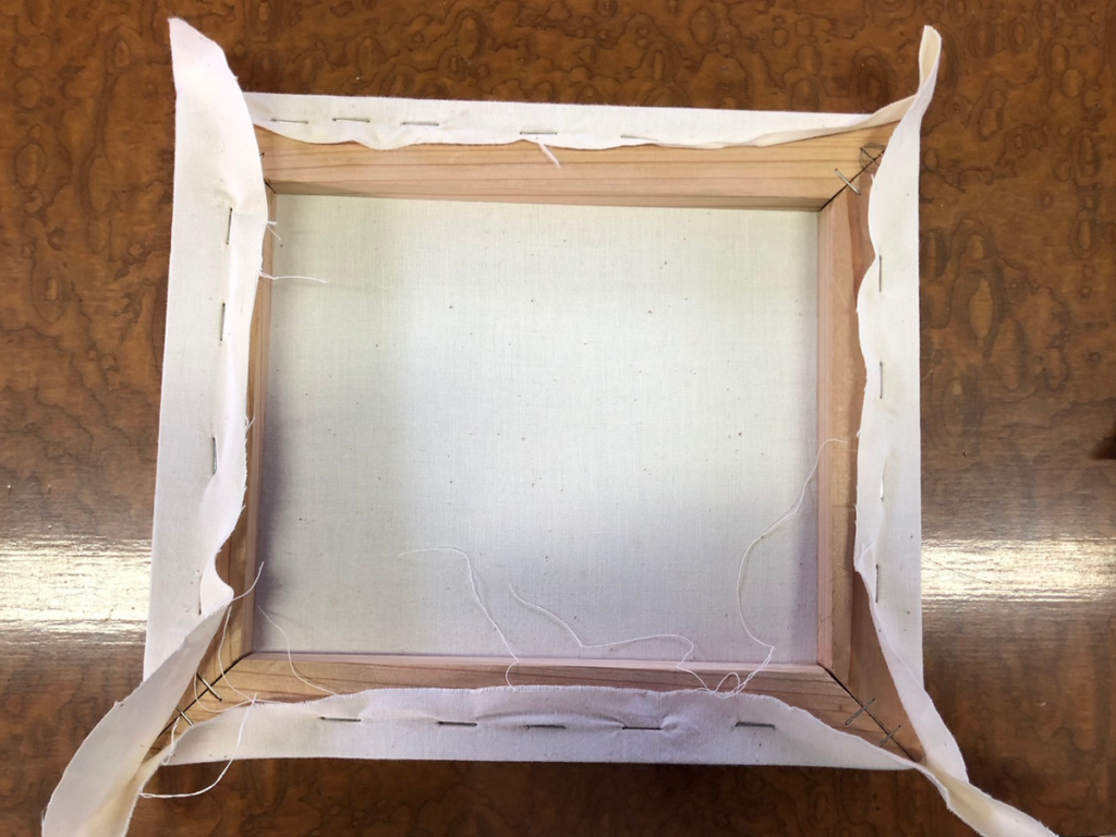 中央から角に向かって、左右交互にタッカーを打ち込み辺を埋めていく様子。シワが寄らないよう均一に固定を進めている工程。